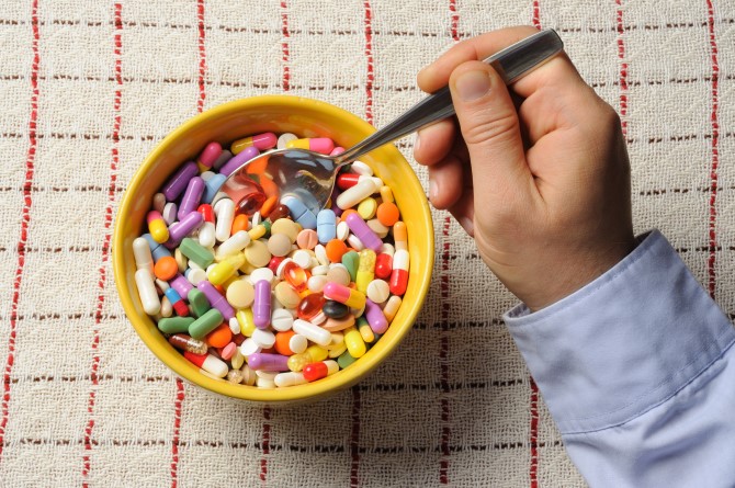 Bowl filled with pills and hand with spoon on a table